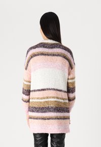 Oversized stickad tröja med horisontella ränder i rosa, vitt, brunt och mörklila. Har en ribbad krage och en flexibel textur.