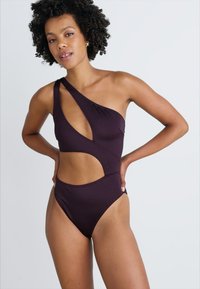 Maillot de bain violet à épaule unique avec design découpé, fabriqué à partir d'un tissu lisse. Présente des accents minimalistes et une taille de jambe haute pour un look moderne.