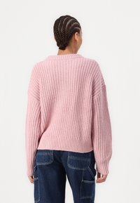 Różowy sweter dziewiarski o luźnym kroju, z prążkowanymi mankietami i dołem. Tekstura jest gruba, podkreślająca swobodny fason z obniżonymi ramionami.