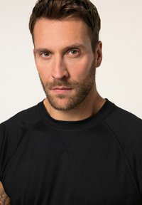 Camiseta deportiva negra con cuello redondo y mangas raglán. Textura suave, tejido ligero, detalles de costura mínimos y diseño ajustado.