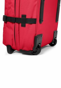 Red wheeled suitcase with a fabric exterior, black plastic accents, a side strap, and four durable black wheels for easy mobility.