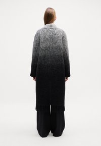 Cappotto in lana grigio ombre con orlo frangiato, dotato di colletto e vestibilità comoda. Il cappotto sfuma da grigio chiaro a nero.
