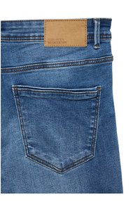 Poche arrière d'un jean en denim bleu avec des surpiqûres orange visibles et une étiquette en cuir beige portant l'inscription "VERO MODA WE DO DENIM".