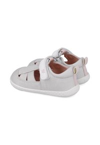 Sandalias de tela gris con una textura suave, puntera cerrada, lados abiertos y correa de Velcro. Presentan acentos en rosa en el talón y el forro interior.