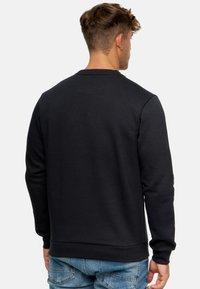 Sudadera gris oscuro con escote redondo, mangas largas y puños acanalados. Textura suave y diseño simple y sólido. Combinada con jeans azules.