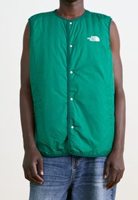 Chaleco sin mangas acolchado verde con botones a presión, que presenta un logotipo en blanco en el lado izquierdo del pecho. Material texturizado e insulated, ajuste casual.