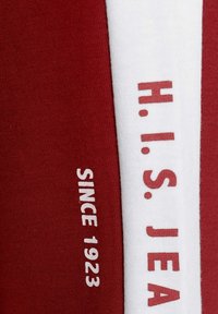 Red fabric shirt featuring white side accents and text reading "H. I. S. JEAN" and "SINCE 1923." Soft texture, casual design.