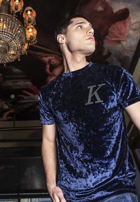 Tmavě modré sametové tričko s krátkým rukávem, s kamínkovou aplikací písmene "K" na levém prsu. Hladký materiál a přiléhavý střih.