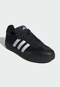 Czarne buty sportowe wykonane z teksturowanej tkaniny, z trzema białymi paskami po bokach, wyściełanym kołnierzem i wzorzystą gumową podeszwą.