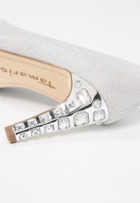 Escarpin argenté pailleté avec un dessus en tricot texturé et un talon métallique orné de pierres précieuses claires rectangulaires et rondes.