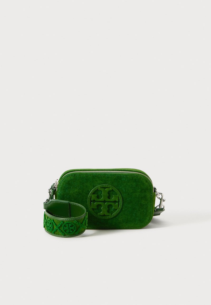 Zeleni platneni crossbody torbica sa kružnim logotipom, zatvaranjem na zip, i podesivim remenom sa izvezenim detaljima. Kompaktna i pravokutna forma.