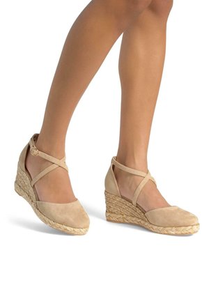 Beige suède wedge schoenen met kruislings enkelbandjes en geweven stro-achtige detailing op de hak. Rond neuzenontwerp.