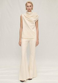 Cream-colored sleeveless top with draped neckline, paired with flared cream trousers. Smooth texture, minimalist design, and coordinated colors.