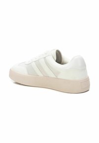 Zapatilla blanca con parte superior de cuero liso y textil, que presenta tres acentos a rayas, una puntera redondeada y una suela de goma beige texturizada.