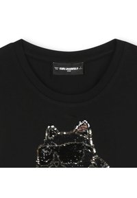 Czarny t-shirt z cekinowym wzorem kota w odcieniach czerni, złota i brązu, w okularach przeciwsłonecznych. Okrągły dekolt i miękka faktura materiału.