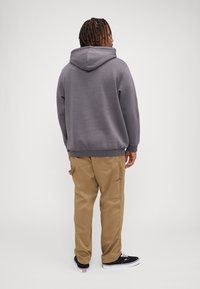 Grå hettegenser med kengurulomme, ribbede mansjetter og kant. Tan cargo-bukser med sidelommer. Sorte sneakers med hvite såler.