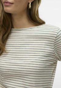 Crème en marine gestreepte blouse met een ronde halslijn, van zachte katoen met een gladde textuur. Gouden golvende creolen zijn zichtbaar.