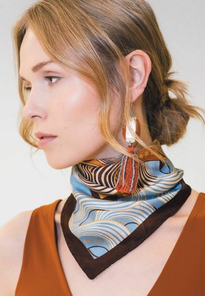Donna con capelli castano chiaro raccolti in un basso chignon, che indossa una sciarpa al collo con motivi blu, marrone e arancione e un grande orecchino con parte superiore bianca e nappina arancione.