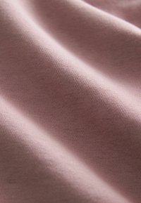 Tejido de algodón suave en color rosa, con una textura lisa que presenta un fino patrón acanalado. El material cae suavemente, destacando su naturaleza liviana.