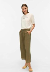 Camiseta crema con texto, pantalones anchos verde oliva y sandalias de tacón amarillas. La camiseta tiene un ajuste casual, los pantalones cuentan con una cinturilla elástica.