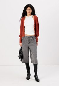 Rustfarget ribbestrikket cardigan, hvit tank topp, grå vid benjeans, og svarte knelange støvler. Tilbehøret inkluderer en svart håndbag.