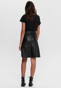 Sort læderskørt med en udtragende design, glat tekstur og lynlåsdetalje på ryggen, parret med en sort t-shirt med korte ærmer og støvler.