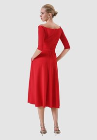 Vestito rosso con maniche a tre quarti e scollo a barca. Tessuto liscio, corpetto aderente, gonna svasata e tasche laterali.