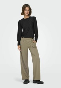 Top nero a maniche lunghe con motivo testurizzato, abbinato a pantaloni beige a gamba larga con tasche laterali e scarpe nere basse.