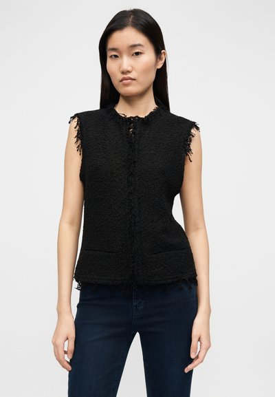 Colete preto sem mangas com bordas desfiadas, tecido texturizado, fecho frontal com botões e dois bolsos laterais, combinado com jeans escuros.