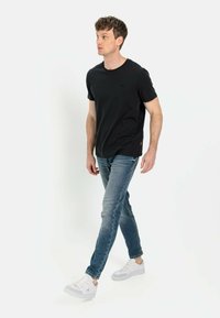 Sort bomulds T-shirt med rund halsudskæring og kortærmede, parret med falmede blå jeans og hvide sneakers, set fra siden.