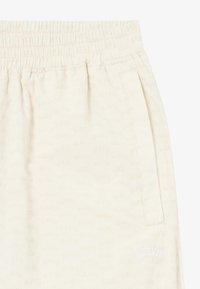 Shorts beige clair avec une taille élastique, présentant un motif subtil en logo BLKVIS sur l'ensemble et des poches latérales.