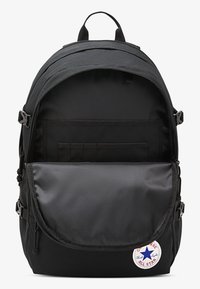 Svart ryggsekk med en stor glidelåsåpning, innerlommer og klaff på forsiden. Har en Converse All Star-merkelapp og slitesterkt stoff.