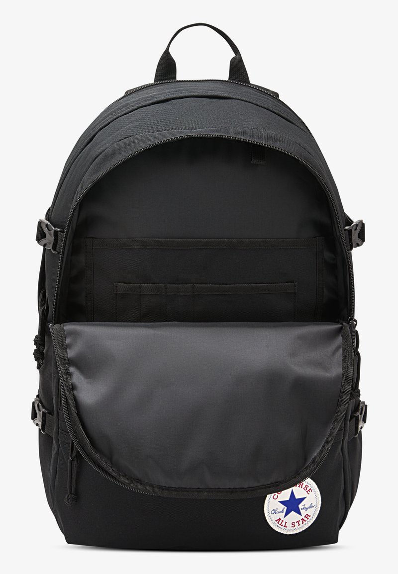 Sort rygsæk med en stor lynlåsåbning, inderlommer og en frontklap. Har et Converse All Star-patch og slidstærkt stof.