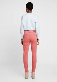 Jeans ajustados rosas con bolsillos traseros, combinados con una camiseta corta de color azul claro. La camiseta presenta un detalle de pliegue y puños con botones.