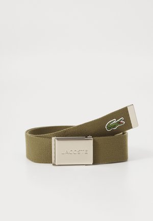 Ceinture élastique vert olive avec une boucle métallique argentée, présentant une surface texturée et un petit logo de crocodile brodé.