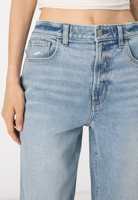 Jeans din denim de culoare albastru deschis, cu o croială relaxată, având închidere cu nasture, buzunare frontale și o ușoară decolorare. Accente uzate lângă buzunar.