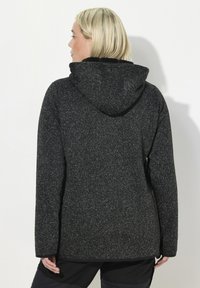 Giacca nera in pile con cappuccio, caratterizzata da un design texturato e maculato e un taglio dritto. Maniche lunghe e una finitura morbida.