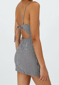 Sort-hvid ternet ærmeløs kjole med tætsiddende silhuet, åben ryg og justerbar knytning i taljen.