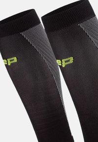 Calze compressive nere con una finitura testurizzata, caratterizzate da dettagli grigi e un logo verde lime sul lato. Design liscio e aderente.