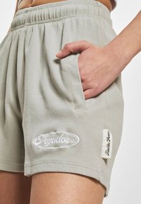 Gaišpelēka kordūru šorti ar elastīgu jostu, sānu kabatām un izšūtu logotipa detaļu uz kājas. Mīksta tekstūra, brīva piegriezuma stils.
