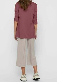 Haut mauve à manches longues, coupe ample, associé à un pantalon à jambes larges beige clair. Chaussures avec des détails de couleur claire et une semelle épaisse.
