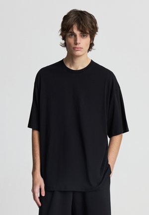 Czarna, krótki rękaw t-shirt wykonany z miękkiej tkaniny, o luźnym kroju i okrągłym dekolcie, z gładką fakturą i minimalistycznym designem.