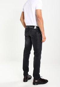 Jeans de denim negro con un ajuste Slim, diseño estándar de cinco bolsillos y una textura suave. Combinados con una camiseta blanca sencilla y calzado negro.