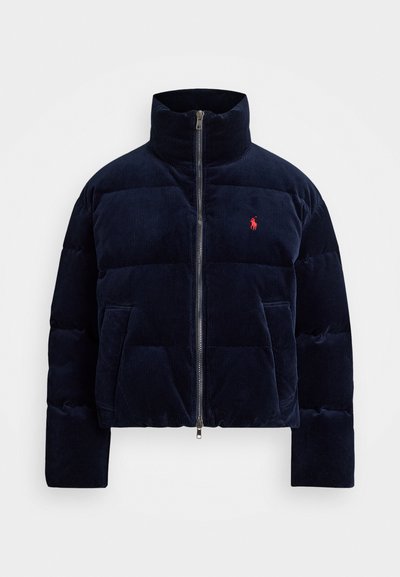 Veste en duvet en velours côtelé bleu marine avec un col haut, fermeture éclair et détail logo rouge sur la poitrine. Comprend des sections matelassées et des poches latérales.