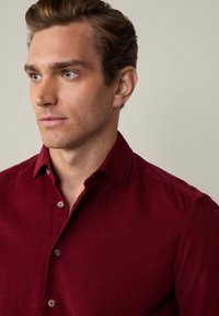 Camicia button-up bordeaux con colletto a punta, realizzata in tessuto morbido, con bottoni arrotondati e dettagli di texture sottili.