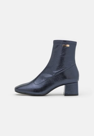 Marineblauwe enkellaarzen gemaakt van glanzend materiaal, met een spitse neus en een vierkante hak. Gladde textuur met minimale stikseldetails.