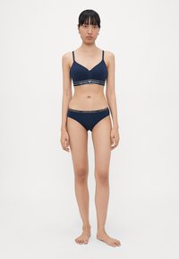 Mornarsko modra bralette in bikini komplet z nastavljivimi naramnicami. Vključuje elastičen pas z logotipom "Emporio Armani" na obeh delih. Gladka tekstura.