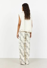 Top fără mâneci, de culoare crem, asortat cu pantaloni largi, cu un model crem și un design abstract negru. Textură netedă a stofei pe toată suprafața.