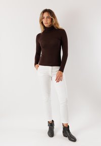 Maglione a maniche lunghe marrone con collo a imbuto abbinato a pantaloni bianchi aderenti e stivaletti neri alla caviglia con cerniere. Tessuto morbido, design aderente.