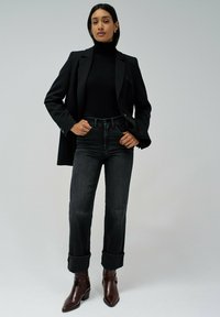 Črn krojen suknjič, črna turtleneck majica, temno jeans hlače s zavihanimi robovi in rjavi usnjeni gležnjarji s koničastim nosom.